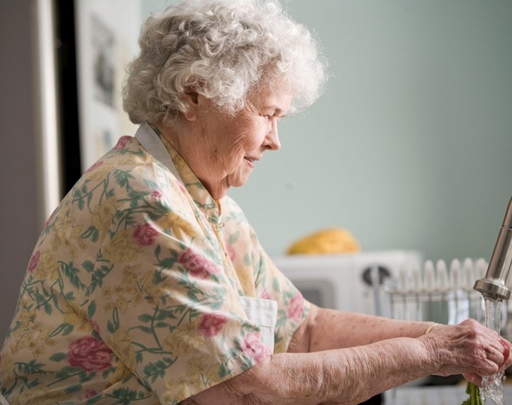 Senior woman washing up dishes at kitchen sink