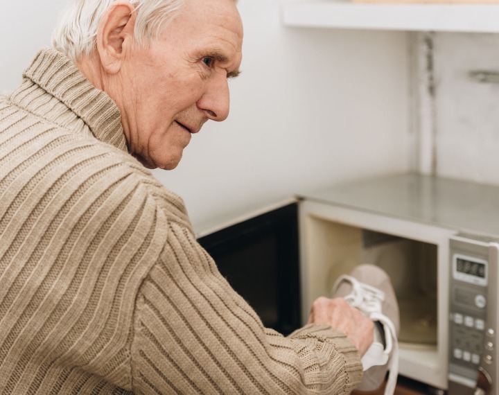 Confused senior putting trainer in microwave